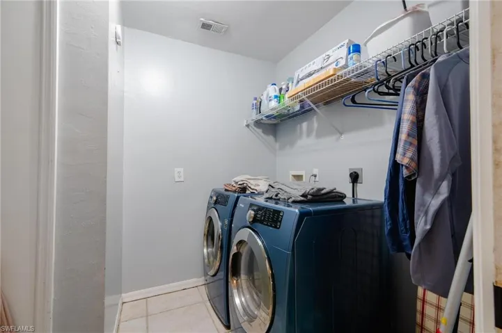 Washroom with washing machine and dryer and light tile patterned flooring