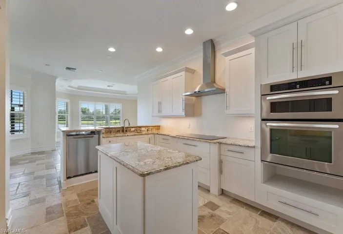 Kitchen with wall chimney range hood, recessed lighting, crown molding, appliances with stainless steel finishes, and stone tile floors
