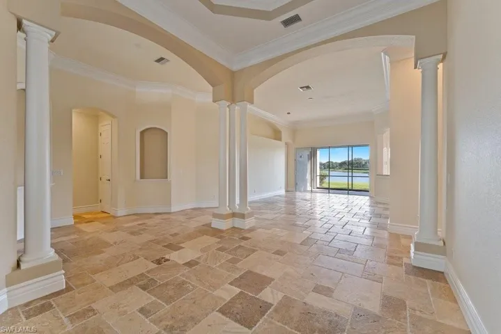Unfurnished room with crown molding, visible vents, baseboards, and stone tile flooring
