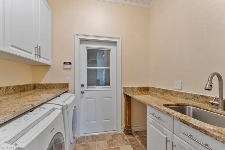 Clothes washing area featuring separate washer and dryer, a sink, stone finish floor, crown molding, and cabinet space