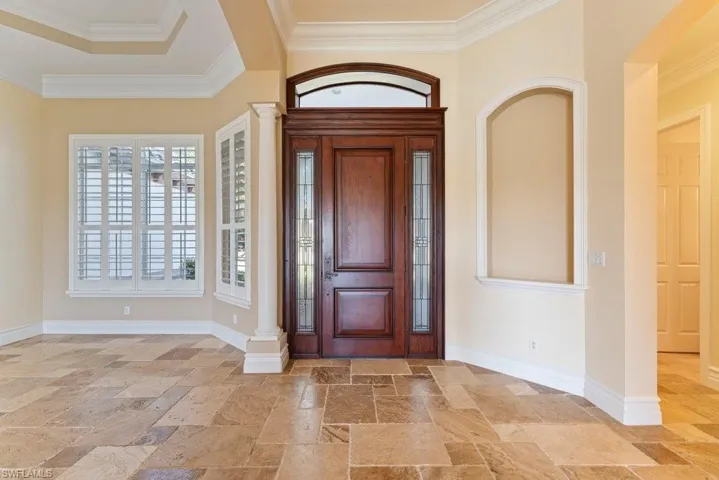 Foyer with crown molding, baseboards, ornate columns, and stone tile floors