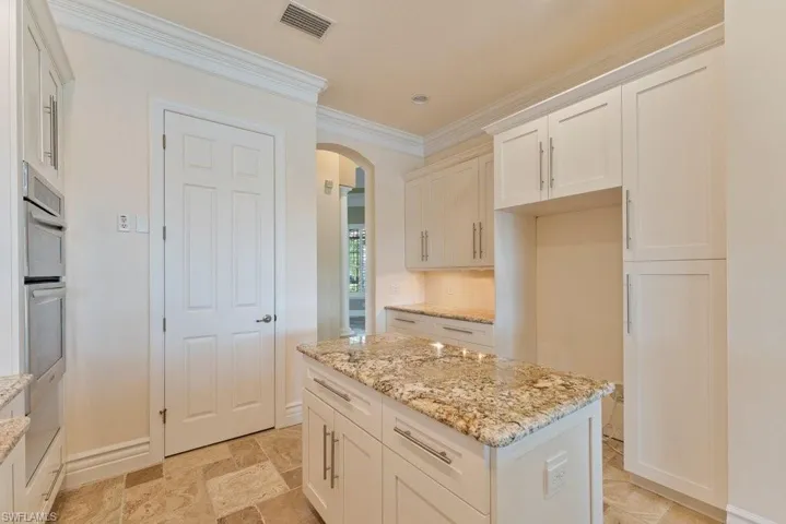 Kitchen featuring visible vents, arched walkways, crown molding, white cabinetry, and light stone countertops