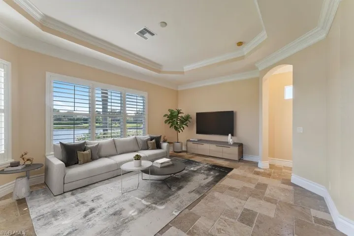 Living area with a tray ceiling, arched walkways, ornamental molding, and visible vents