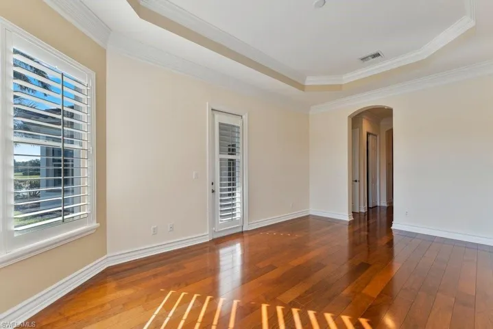 Empty room featuring arched walkways, visible vents, hardwood / wood-style flooring, and ornamental molding