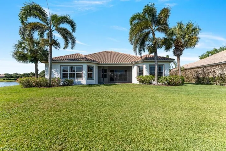 Back of house with a sunroom, a tiled roof, a water view, a lawn, and stucco siding