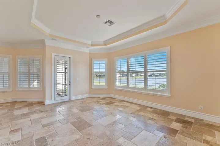 Spare room featuring stone tile floors, visible vents, a tray ceiling, and crown molding