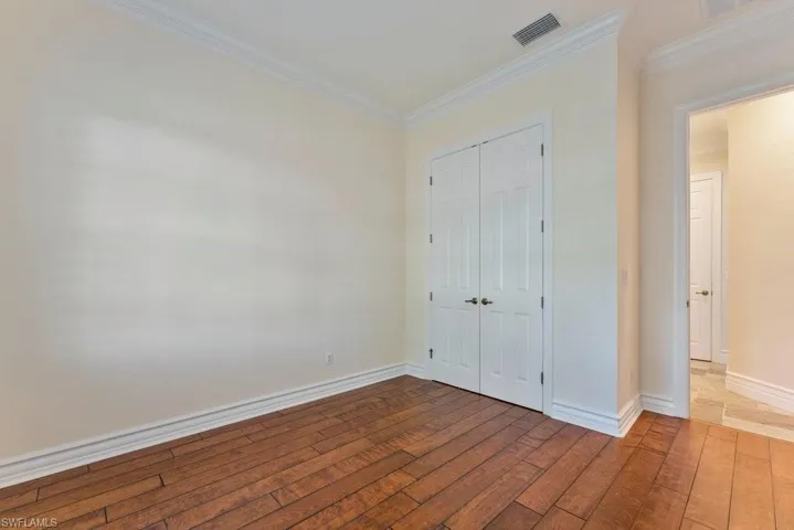 Unfurnished bedroom featuring crown molding, visible vents, a closet, and hardwood / wood-style flooring