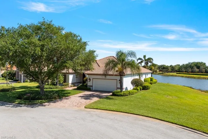 View of front of home featuring a water view, a tiled roof, a garage, stucco siding, and a front lawn