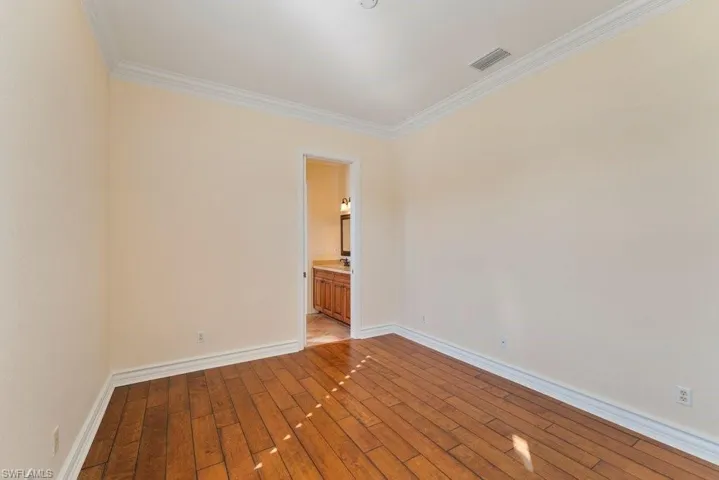 Spare room with crown molding, light wood finished floors, baseboards, and visible vents