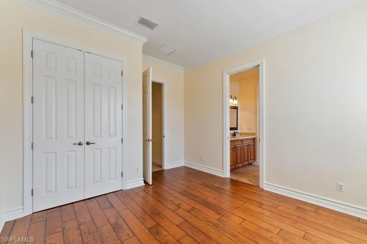 Unfurnished bedroom featuring baseboards, a closet, crown molding, visible vents, and wood-type flooring