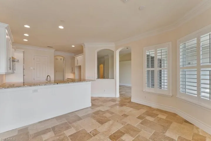 Kitchen featuring crown molding, light stone counters, white cabinets, and stone tile floors