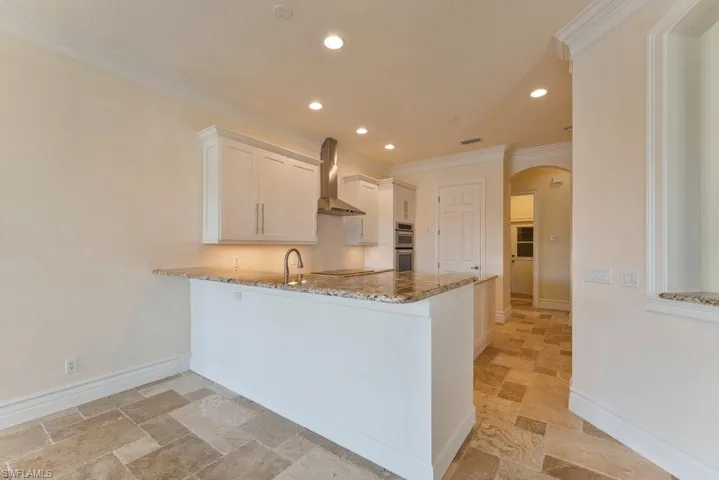 Kitchen featuring arched walkways, ornamental molding, light stone counters, black electric stovetop, and stone tile flooring