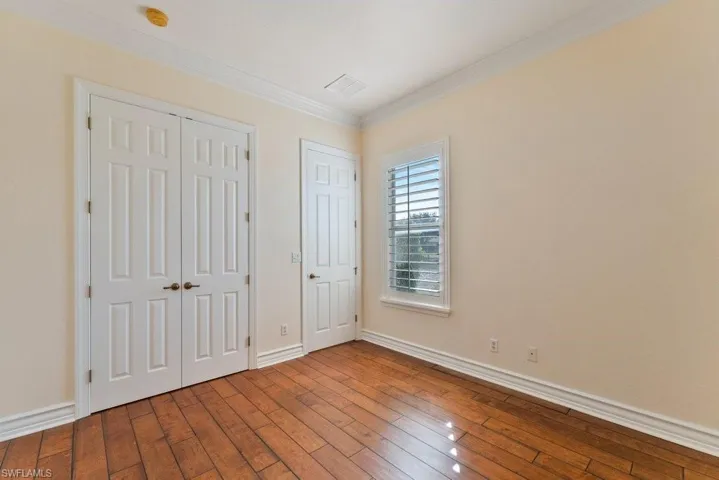 Unfurnished bedroom with visible vents, baseboards, a closet, ornamental molding, and wood-type flooring