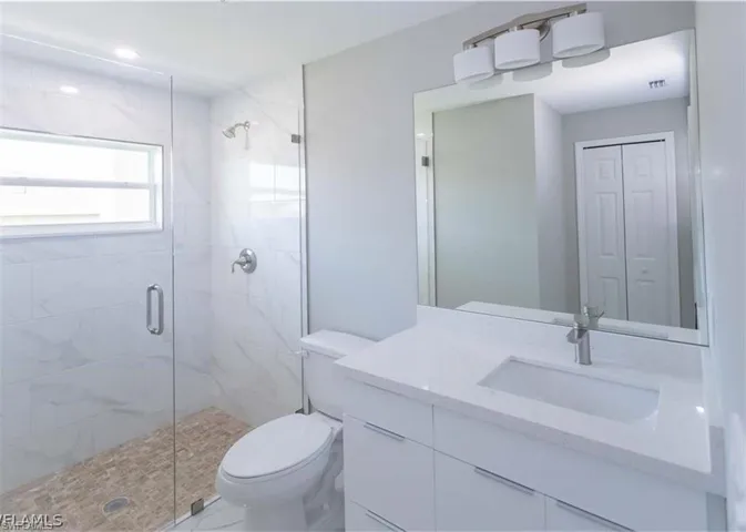 Contemporary bathroom featuring a frameless glass shower enclosure, white marble-look wall tile, and a pebble-style shower floor