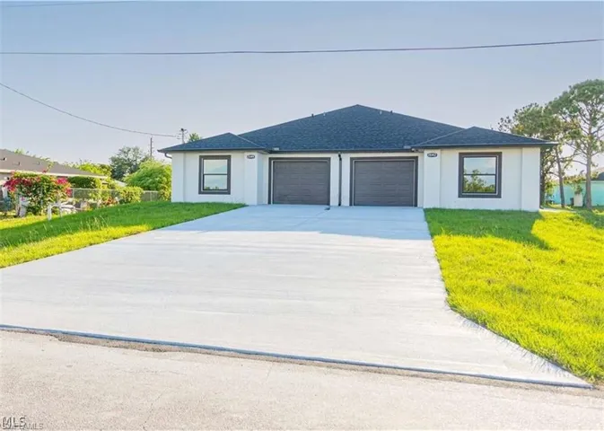 Contemporary duplex building with a dark shingle roof, two distinct garage doors, a large concrete driveway, and surrounding green lawn