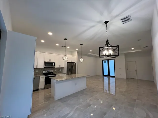 Kitchen with white cabinetry, light stone countertops, decorative light fixtures, a center island, and stainless steel appliances