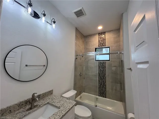 Full bathroom with bath / shower combo with glass door, toilet, and vanity