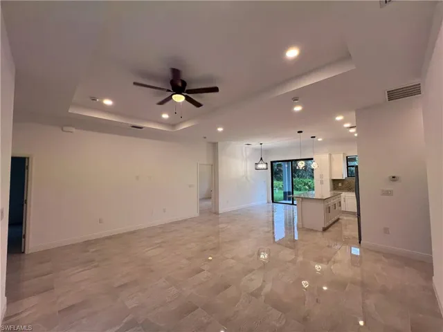 Unfurnished living room featuring a tray ceiling, ceiling fan, and light tile patterned floors