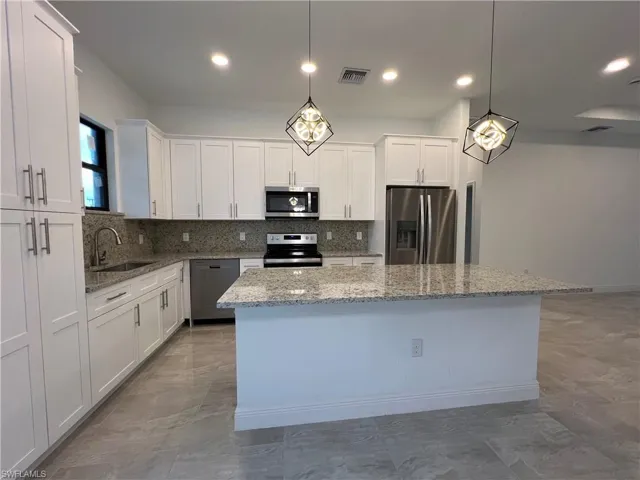 Kitchen featuring backsplash, sink, a kitchen island, stainless steel appliances, and white cabinets