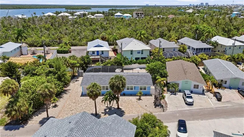 Aerial perspective showcasing a residential area with a prominent light blue single-story home featuring a gray shingle roof and a screened-in pool enclosure - Virtually Edited Image