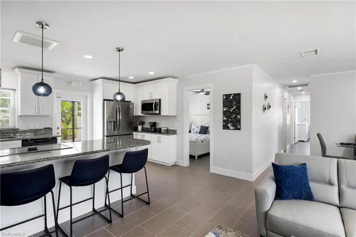 Kitchen featuring open floor plan, dark stone countertops, stainless steel appliances, a breakfast bar, and white cabinets - Virtually Edited Image