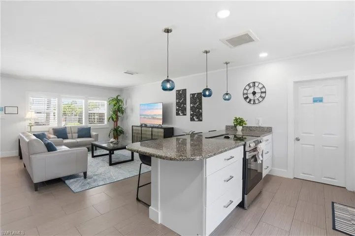 Open-concept living space featuring a kitchen island with granite countertops, stainless steel appliances, and pendant lighting - Virtually Edited Image