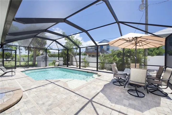 View of swimming pool featuring a lanai, a sunroom, a fenced backyard, a patio area, and a storage unit - Virtually Edited Image