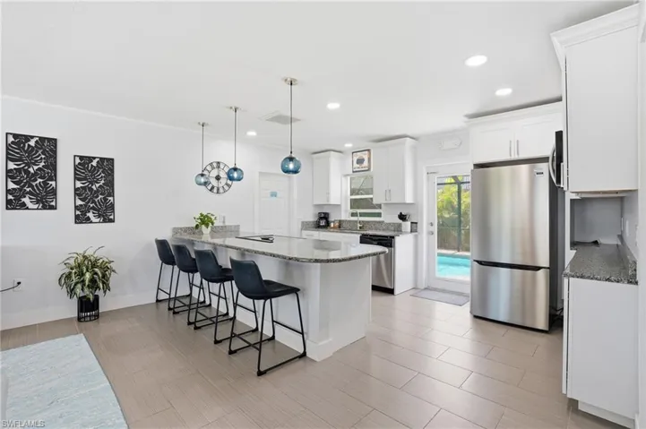 Kitchen featuring an expansive island with seating, white cabinetry, integrated stainless steel appliances, granite countertops, and direct access to an outdoor pool area - Virtually Edited Image