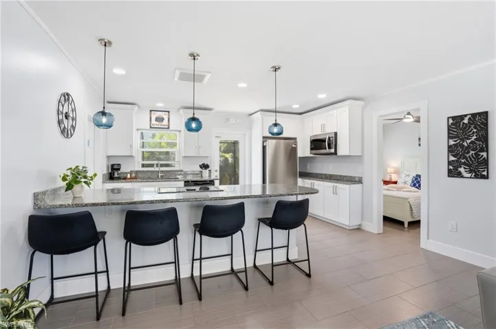 Spacious kitchen featuring an extended peninsula with seating, shaker-style cabinetry, stainless steel appliances, granite countertops, and tile flooring - Virtually Edited Image