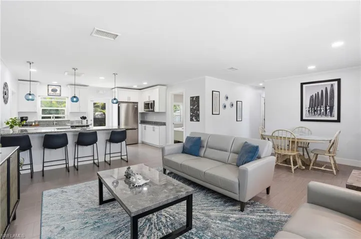 Open-concept living space featuring wood-finish flooring, recessed lighting, and a white color palette - Virtually Edited Image