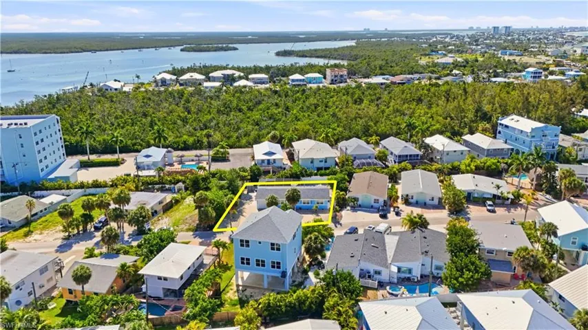 Coastal property featuring a light-colored exterior and a blue roof, situated on a street with mature palm trees