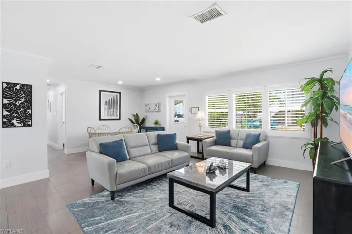 Bright living area featuring wood-finish flooring, white plantation shutters, and recessed lighting - Virtually Edited Image