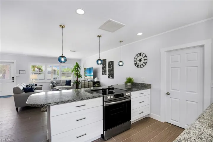Kitchen with dark stone countertops, stainless steel electric range oven, a peninsula, open floor plan, and crown molding - Virtually Edited Image