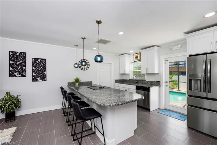Kitchen featuring stainless steel appliances, a peninsula, a breakfast bar area, ornamental molding, and pendant lighting - Virtually Edited Image