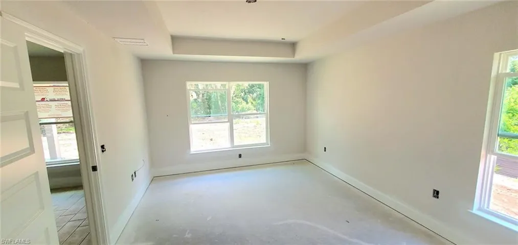 Primary Bedroom featuring a healthy amount of sunlight, concrete flooring, and a raised ceiling