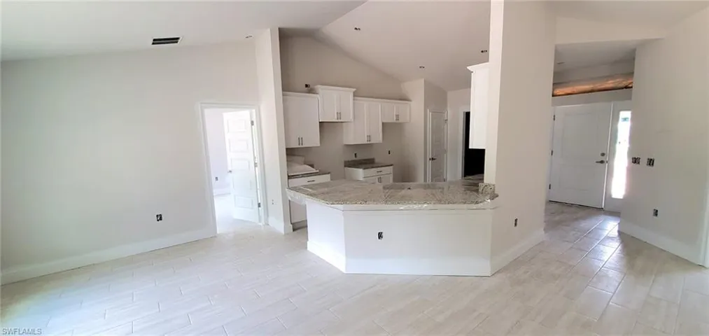 Kitchen with kitchen peninsula, light stone counters, light tile floors, high vaulted ceiling, and white cabinets