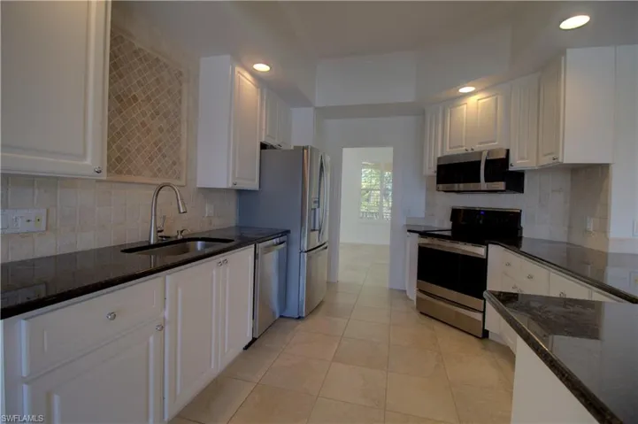 Kitchen featuring dark stone countertops, stainless steel appliances, white cabinetry, recessed lighting, and crown molding