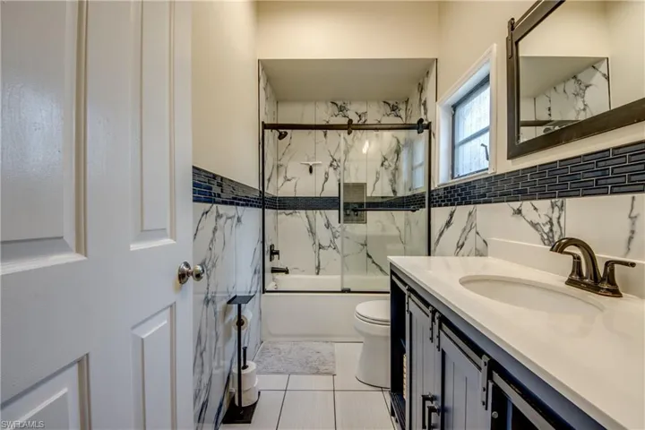 Full bathroom with bath / shower combo with glass door, vanity, tile walls, and light tile patterned flooring