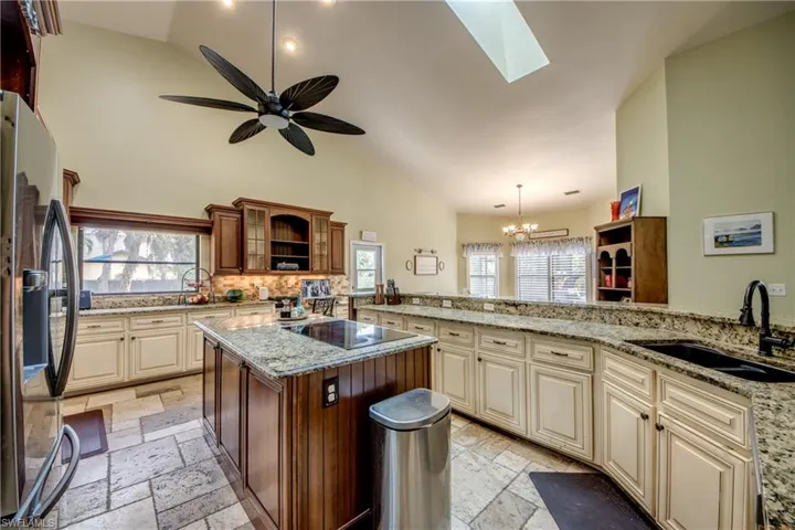Kitchen with cream cabinets, light stone counters, stainless steel fridge with ice dispenser, a skylight, and high vaulted ceiling