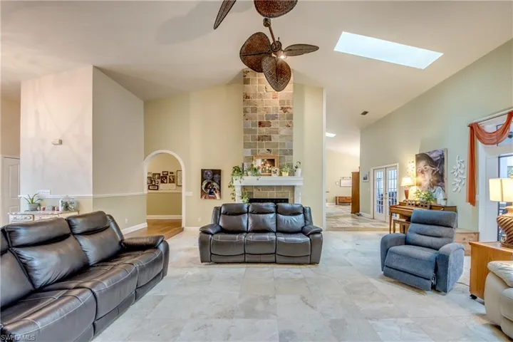 Living room featuring high vaulted ceiling, a skylight, a ceiling fan, a large fireplace, and arched walkways