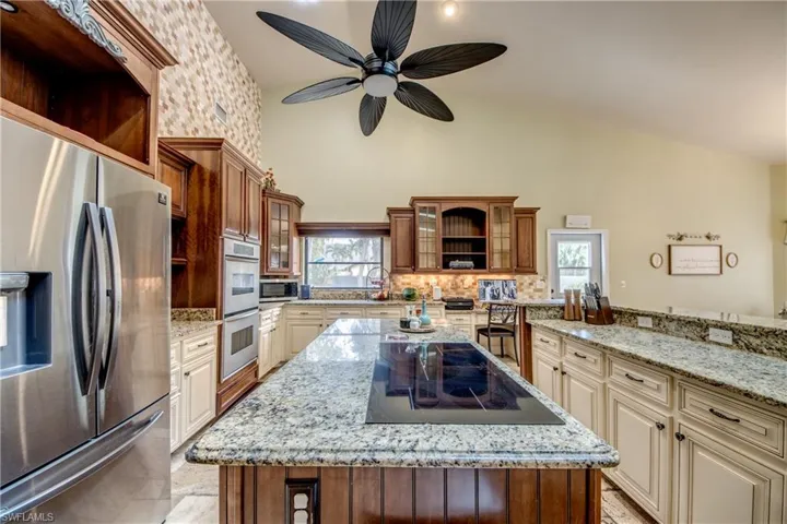 Kitchen with stainless steel appliances, cream cabinetry, light stone countertops, a center island, and open shelves