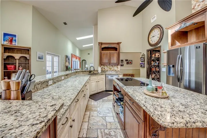 Kitchen with open shelves, brown cabinetry, stainless steel appliances, light stone counters, and high vaulted ceiling