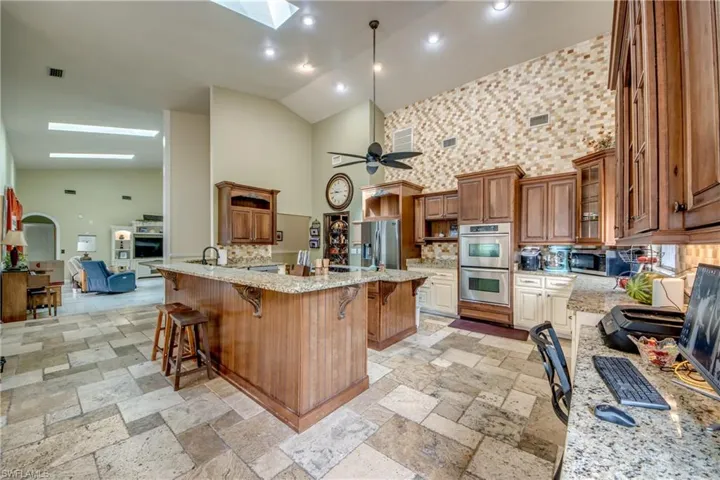 Kitchen with brown cabinetry, a skylight, a breakfast bar, high vaulted ceiling, and light stone countertops