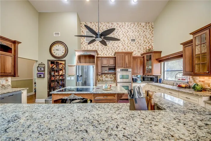 Kitchen featuring backsplash, open shelves, light stone counters, a kitchen island, and a towering ceiling