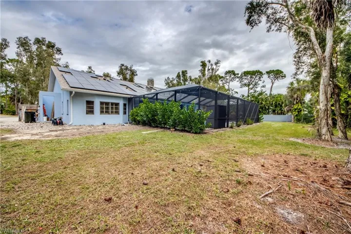 Rear view of property with a lanai, a lawn, roof mounted solar panels, stucco siding, and a sunroom