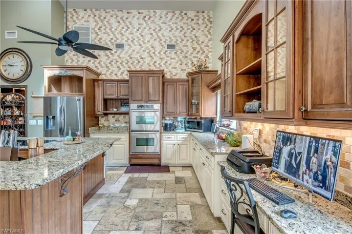 Kitchen with open shelves, brown cabinets, light stone countertops, backsplash, and glass insert cabinets