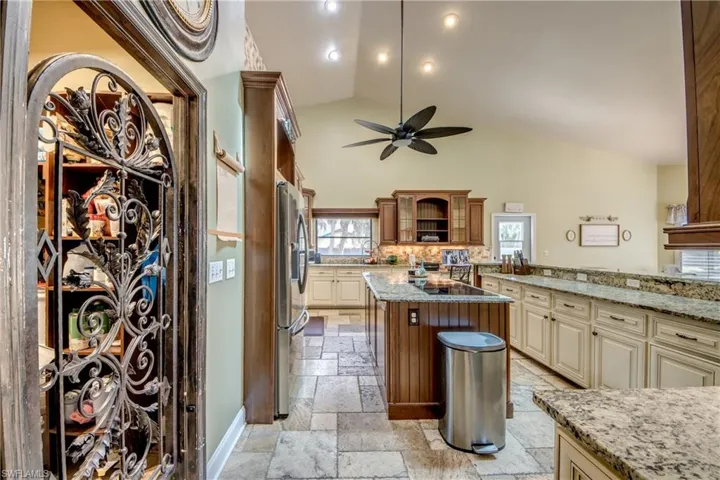 Kitchen featuring cream cabinets, light stone counters, stainless steel refrigerator with ice dispenser, a ceiling fan, and glass insert cabinets