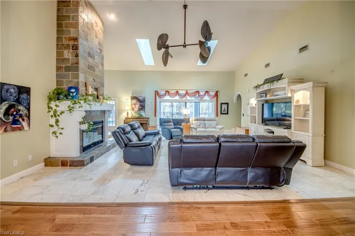 Living room featuring a skylight, light wood finished floors, high vaulted ceiling, a tiled fireplace, and ceiling fan
