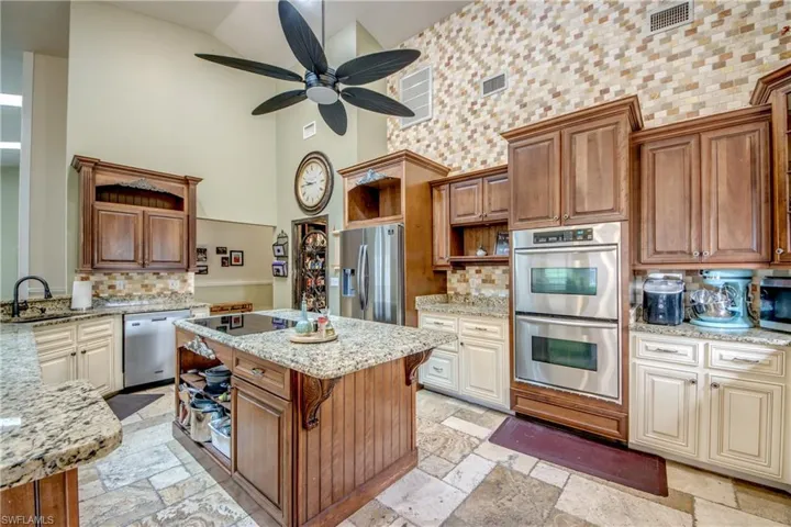Kitchen featuring open shelves, brown cabinets, light stone countertops, appliances with stainless steel finishes, and a high ceiling