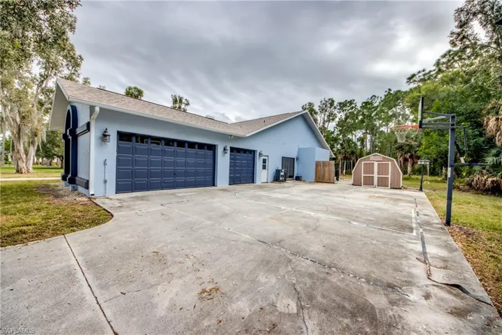 View of side of home with stucco siding, concrete driveway, a garage, and a storage shed